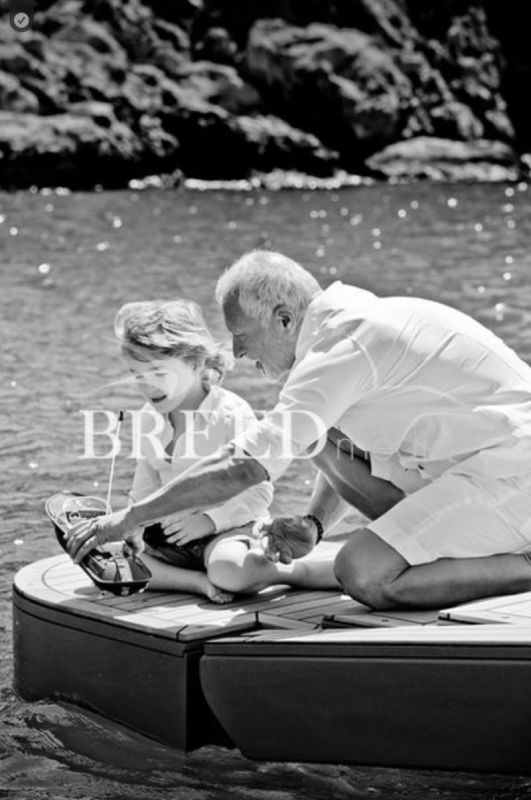 Grandfather and young child playing with a toy boat on a yacht deck at sea