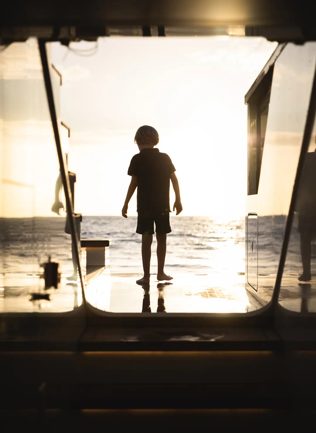 A child standing at the stern of a superyacht at sunset, looking out over the open sea, capturing the private and family-focused lifestyle often associated with superyacht ownership and charter.