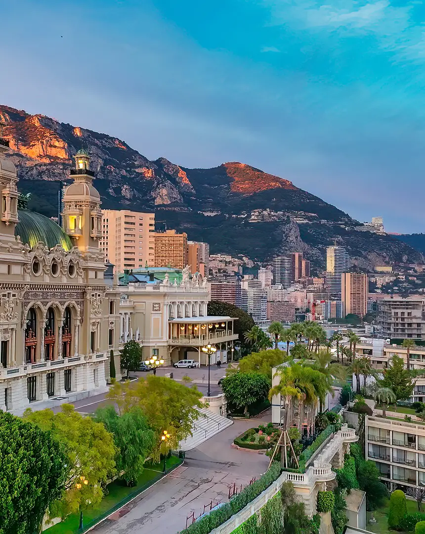 Elegant architectural landmark set against a backdrop of coastal hills and high-rise buildings at sunset, capturing the refined atmosphere associated with global superyacht destinations.