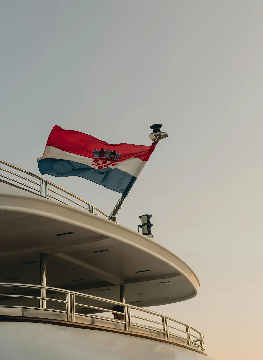 Croatian flag flying from the stern of a superyacht against a soft sunset sky