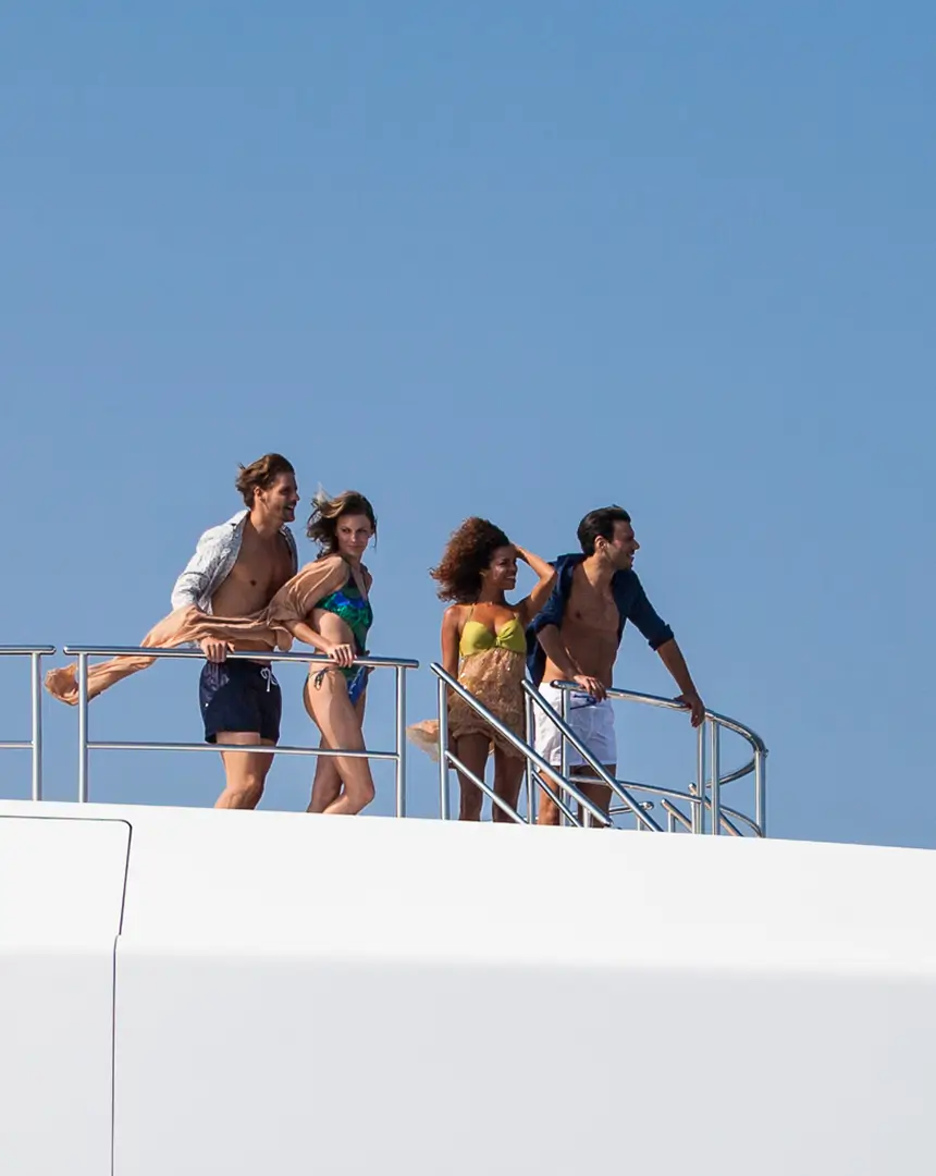 Group of friends standing on the bow of a luxury superyacht, enjoying the sun and sea on a clear blue-sky day.