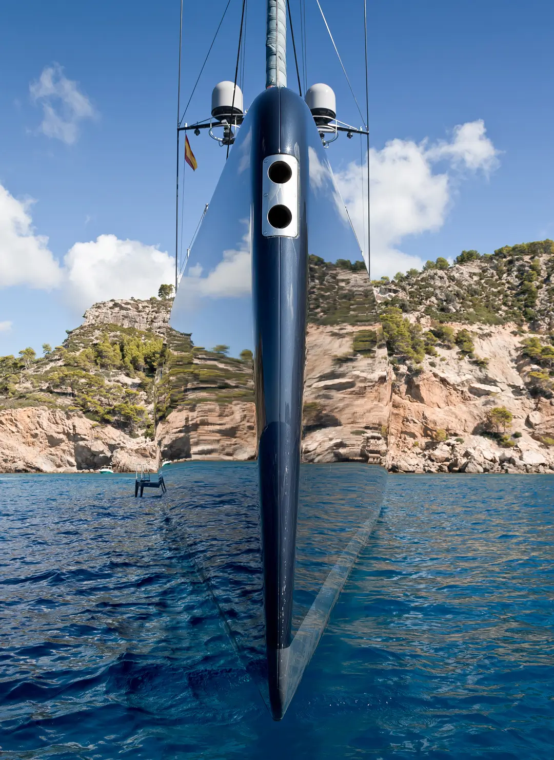 A modern sailing yacht viewed head-on at anchor, showing its sleek reflective hull above deep blue water, suitable for articles about superyacht purchase agreements, new-build oversight, and yacht ownership legal services.