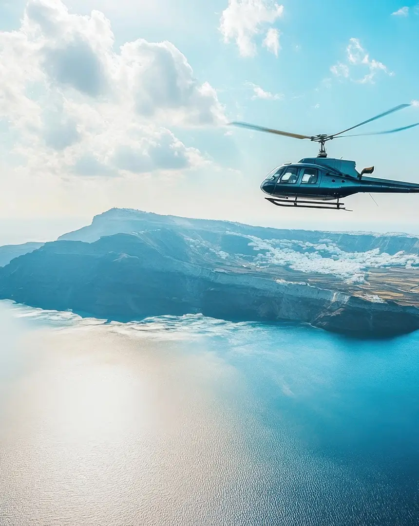 Helicopter flying over a bright blue coastline and volcanic cliffs under a clear sky, capturing the luxury travel lifestyle associated with superyachts.