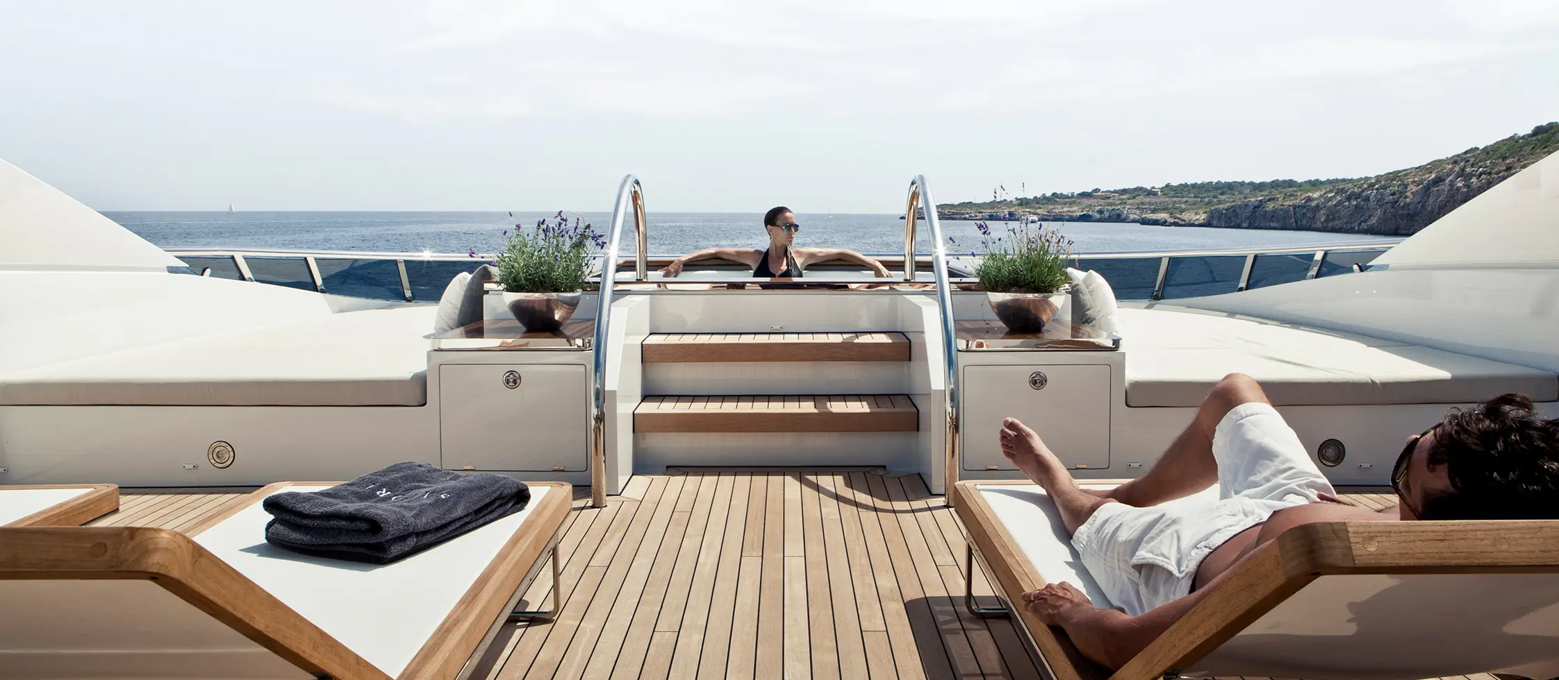 Ownership structuring 1 A woman sitting by a yacht’s upper deck pool with another person lounging on a sunbed.
