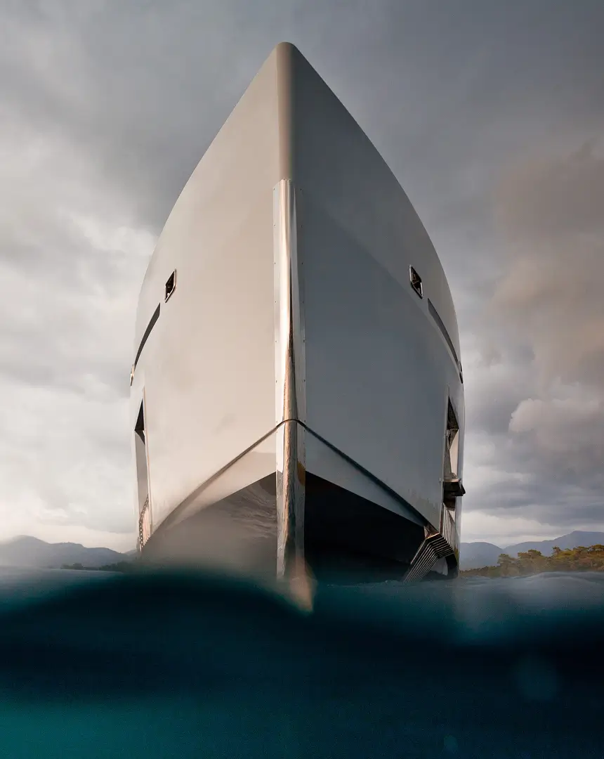 Bow view of a sleek modern superyacht captured at water level, shot against a dramatic sky and calm sea, reflecting the high-end maritime focus of Teji | Cowie.
