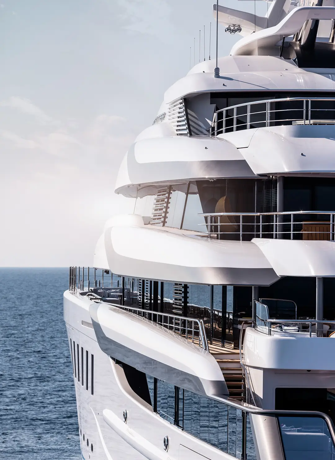 Sleek multi-deck superyacht exterior showcasing curved white terraces and glass railings on open water.