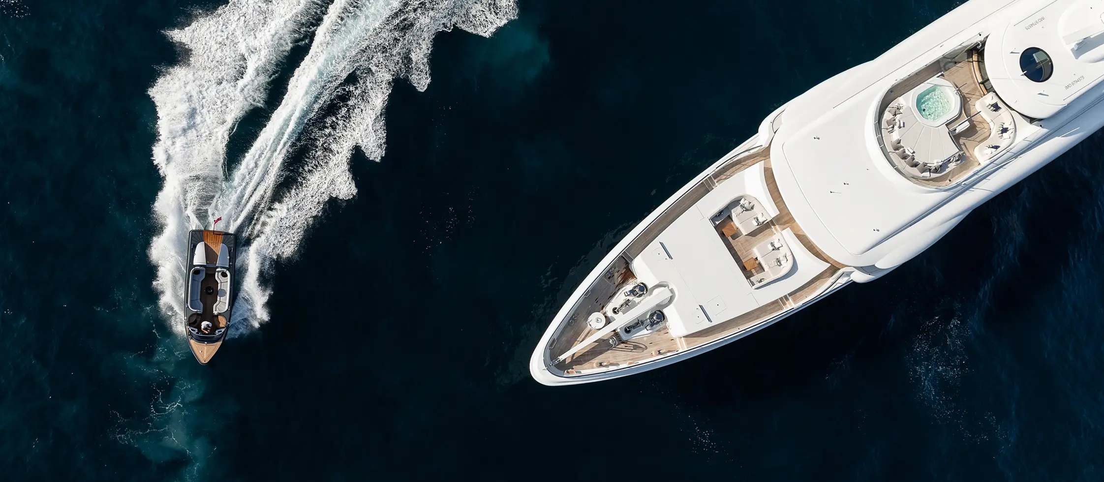 Aerial view of a luxury superyacht cruising alongside a fast tender boat on deep blue water, showcasing yacht bow design and water-sports lifestyle.