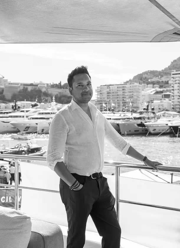 Professional portrait of a man standing on a yacht deck with a marina, superyachts and waterfront buildings in the background