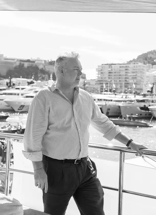 Professional portrait of Antony Cowie standing on a yacht deck overlooking a marina with superyachts and waterfront buildings in the background